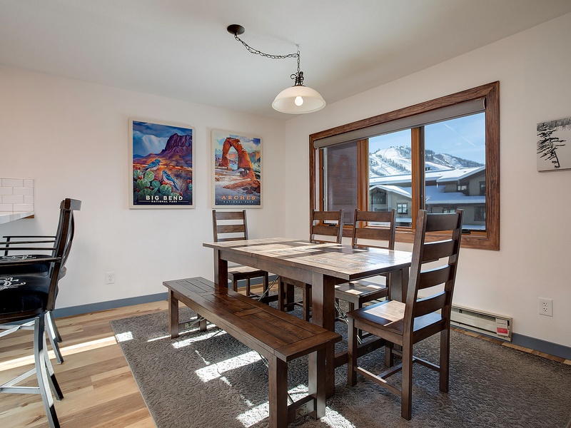 Gather around this inviting dining table where sunlight spills across warm wood floors. The mountain views through the window create a stunning backdrop for your morning coffee and shared meals.