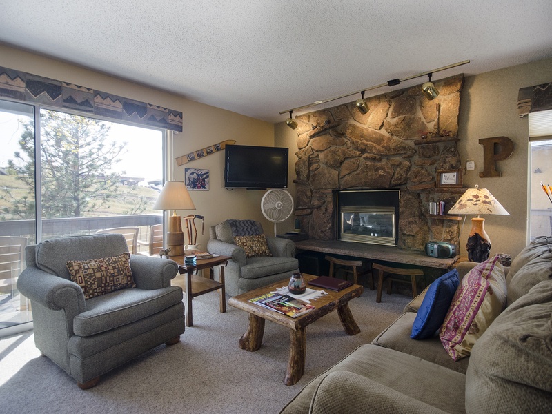Unwind in your cozy living room with a crackling fireplace, plush seating, and warm mountain views framing the windows—perfect for relaxing after a day of adventure.
