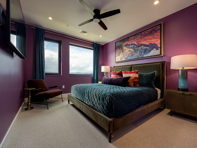 Relax in this thoughtfully designed bedroom with rich purple walls, a ceiling fan, and vibrant decor—your perfect retreat after a day of adventure.