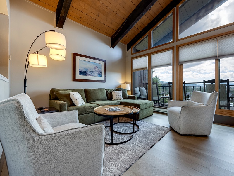 Sink into comfortable seating in your bright, open living room, where soaring wood-beamed ceilings and floor-to-ceiling windows frame stunning mountain views from your private balcony.