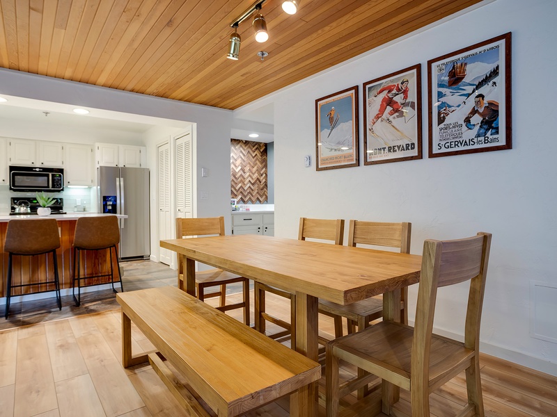 Gather around this inviting dining table for meals and memories, where warm wood tones, vintage ski posters, and a fully equipped kitchen create your perfect mountain retreat.