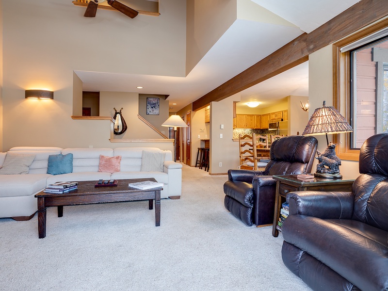 Unwind in your spacious living room where vaulted ceilings with warm wood beams, plush seating, and soft lighting create an inviting retreat after a day of mountain adventure.