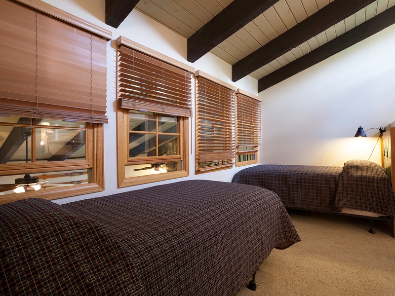 Unwind in your cozy retreat beneath exposed beam ceilings. Two comfortable beds invite restful sleep while warm lighting and wooden blinds create a peaceful mountain escape.