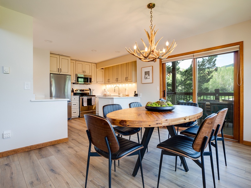 Gather around this inviting round table beneath a stunning antler chandelier, with natural light streaming through doors to your private balcony overlooking green landscapes.