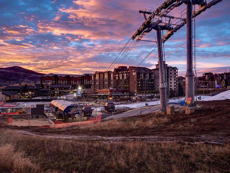 A mountain resort village at dusk, featuring ski lift infrastructure and multi-story lodging buildings set against a dramatic pink and purple sunset sky.