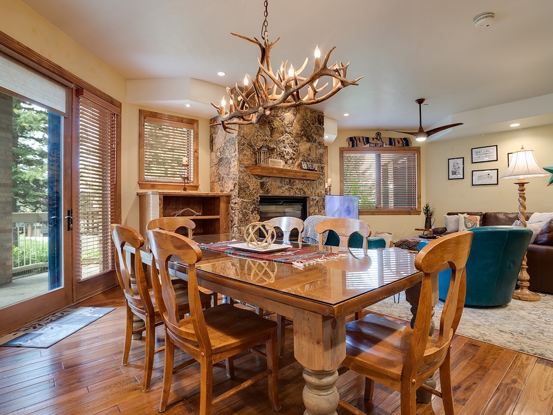 Gather around the rustic dining table under the antler chandelier, where warm wooden tones and a stone fireplace create a cozy mountain retreat for your meals and memories together.