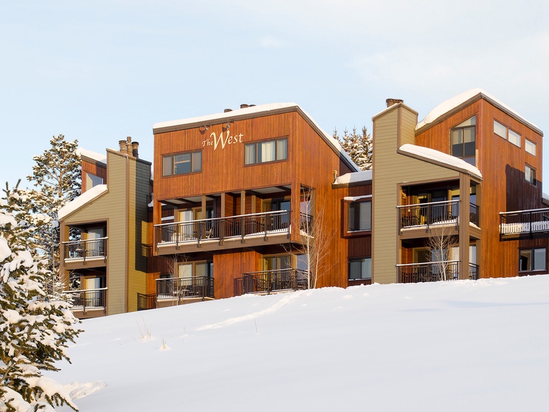 Modern alpine property with warm wood siding nestled on a snowy hillside, featuring multiple balconies and mountain-view access.