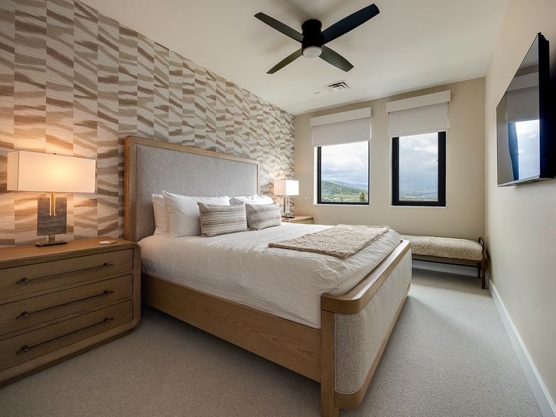 Drift off to peaceful sleep in this serene bedroom, complete with plush linens, a stunning textured accent wall, and windows framing sweeping mountain views that greet you each morning.