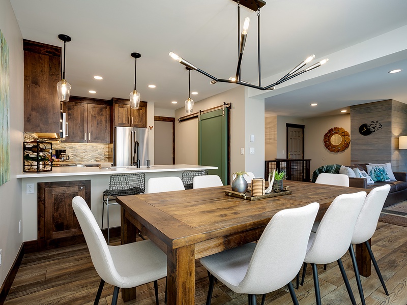Gather around the rustic dining table, where warm wood tones and modern lighting create the perfect space for your meals and conversations, flowing seamlessly into your fully-equipped kitchen and cozy bedroom beyond.