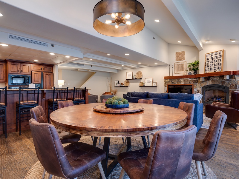 Gather around the stunning round dining table, perfect for lively meals and conversation. Beyond, sink into plush seating by the stone fireplace, where warmth and elegance meet.