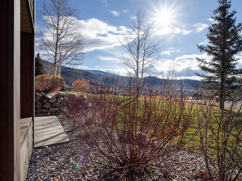 Stunning mountain views frame this vacation rental, with layers of dramatic peaks rising beyond open fields and bare deciduous trees in the foreground—a scenic mountain-side setting.