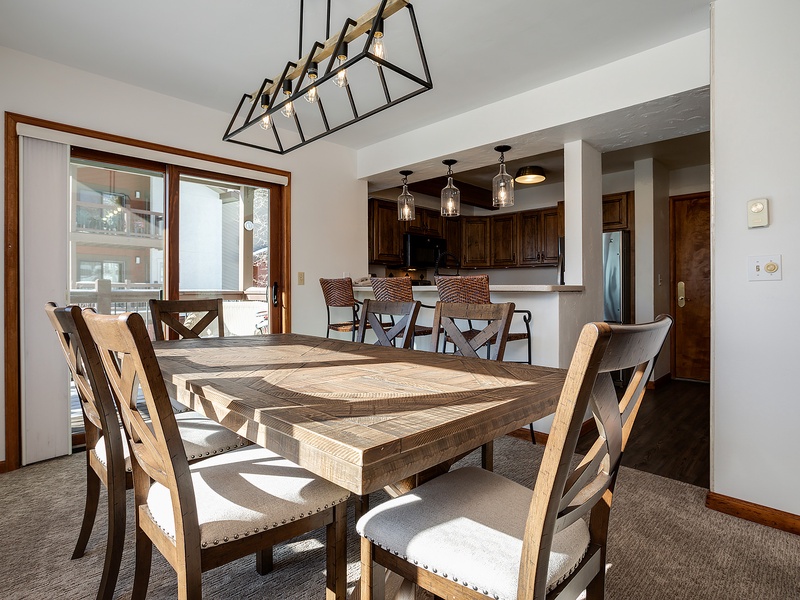 Gather around this rustic dining table where sunlight streams through large windows. The open layout flows seamlessly into a fully equipped kitchen with bar seating, perfect for your group meals and morning coffee.