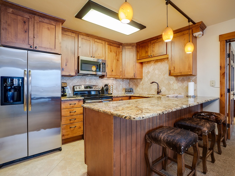 Warm wood tones and granite counters create your inviting kitchen space. Gather around the island, whip up meals with modern appliances, and enjoy the cozy ambiance of pendant lighting overhead.
