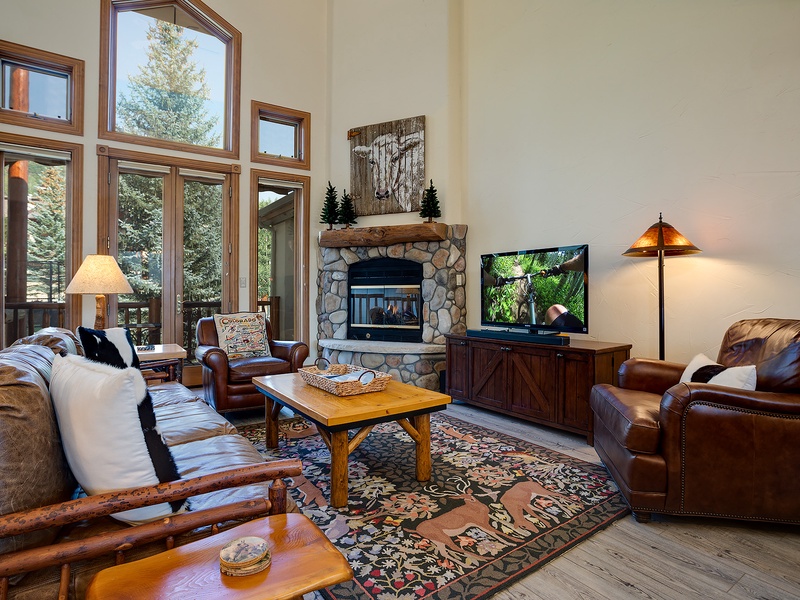 Unwind in your cozy living room, where natural light pours through soaring windows, a stone fireplace adds rustic charm, and comfortable furnishings invite you to relax after a day of adventure.
