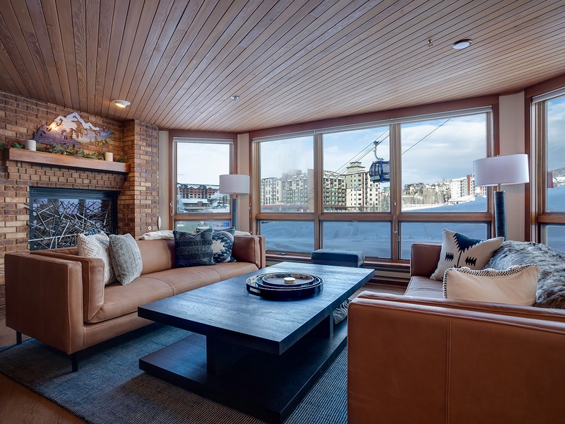 Relax in your mountain-view living room with plush leather seating, a warm fireplace, and floor-to-ceiling windows overlooking the slopes and ski gondola—your perfect alpine retreat.