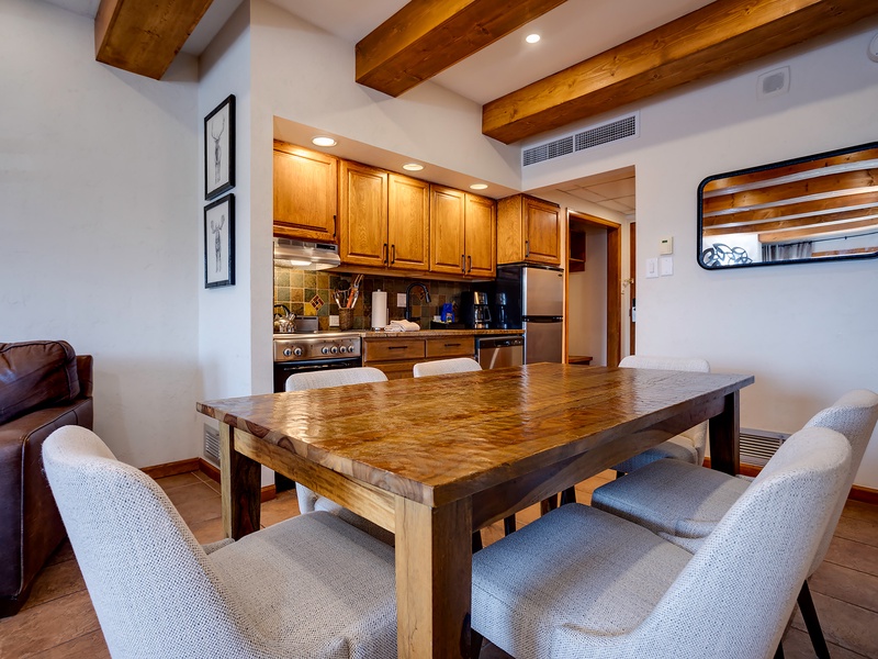 Gather around the handcrafted wood table beneath exposed timber beams. Your fully equipped kitchen awaits with stainless appliances, warm wood cabinetry, and open-concept flow perfect for meals together.