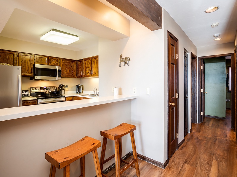 Your open kitchen with breakfast bar and rustic wood stools invites easy mornings, while warm beam accents and natural wood details add a cozy, inviting charm throughout.