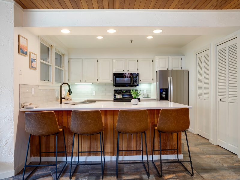 Gather around your bright, modern kitchen where clean lines meet warm wood tones. Four barstools invite you to linger over morning coffee or evening cocktails at the spacious island.