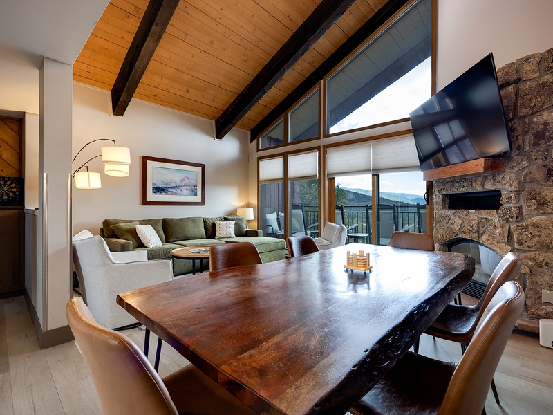Gather around the handsome wood table or relax on the plush sofa—your mountain retreat combines rustic stone and warm beams with sweeping vistas through floor-to-ceiling windows.