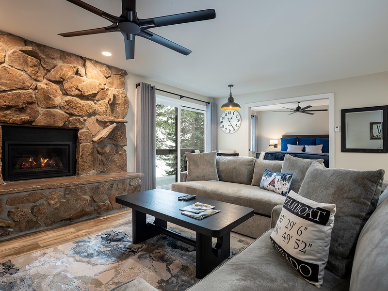 Unwind in your inviting living space with a cozy stone fireplace, plush seating, and ceiling fans. The glass doors frame serene views, while the adjacent bedroom beckons for restful nights.
