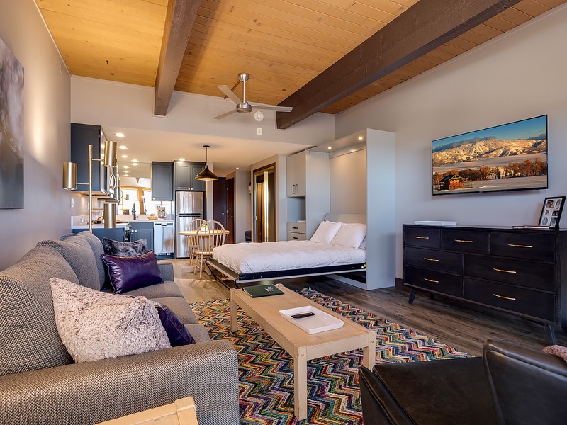 Your open-concept retreat features soaring wood-beamed ceilings, a plush living area, a cozy sleeping nook, and mountain views that remind you of the adventure waiting outside.