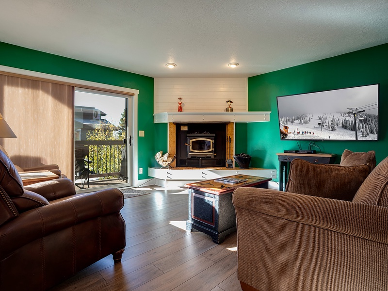 Picture yourself unwinding in this inviting living room, where warm wood tones and bold emerald walls create a cozy alpine retreat. Your balcony opens to scenic views, while the fireplace promises relaxing evenings ahead.