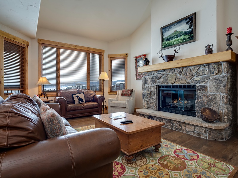 Your inviting living room features a stunning stone fireplace, plush leather seating, and mountain views through expansive windows—perfect for unwinding after a day exploring nearby trails.