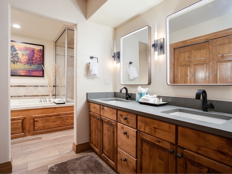 Step into your private retreat with a spacious dual-sink vanity and a soaking tub just beyond. Warm wood tones and modern fixtures create a perfect blend of rustic charm and comfort.