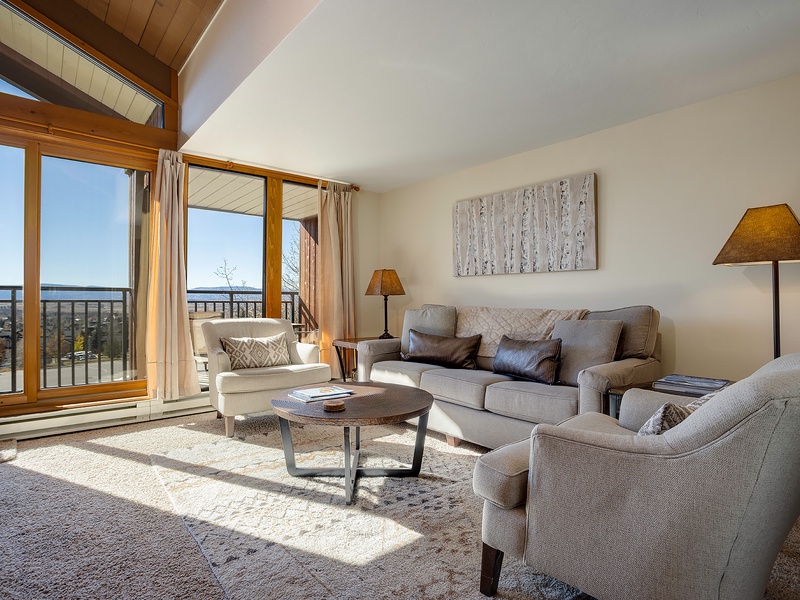 Sink into plush seating as natural light fills your living room, where vaulted ceilings and panoramic balcony views create your perfect mountain retreat.