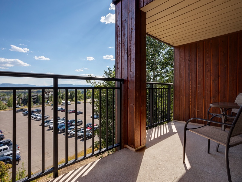 A balcony offering mountain vistas and open skies, with seating for relaxation. The property is situated in a neighborhood area with parking facilities nearby.