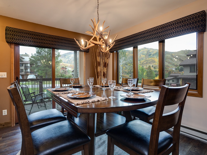 Gather around this warm dining space where mountain views frame every meal. The rustic antler chandelier and rich wood tones create a cozy mountain retreat feel, perfect for your group dinners and morning coffee.