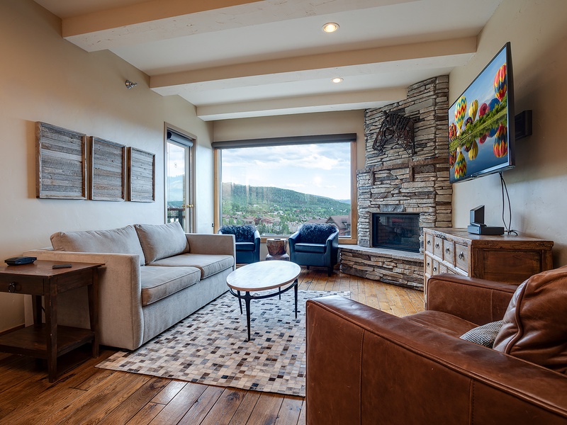 Unwind in your spacious living room where a stone fireplace adds warmth and floor-to-ceiling windows frame breathtaking mountain views—your perfect retreat after exploring the area.