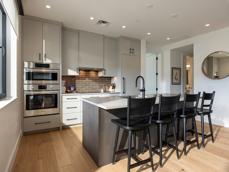 Your modern kitchen invites you to gather around the sleek island for morning coffee or casual meals, with gleaming stainless-steel appliances and warm wood floors underfoot.