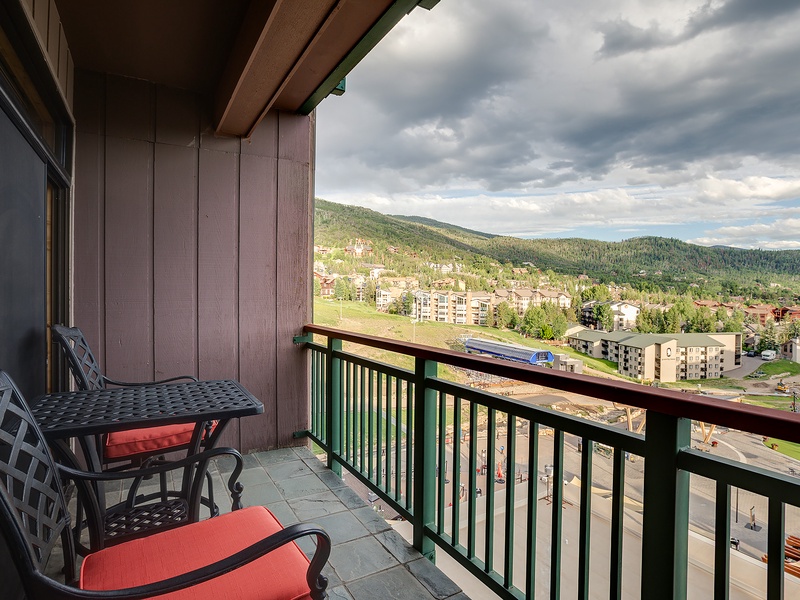 Sweeping mountain and valley vistas frame this private balcony retreat, where forested peaks meet charming alpine architecture below dramatic skies.