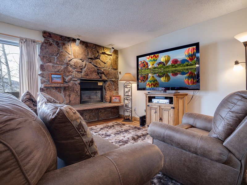 Unwind in your cozy living room with plush seating, a warm stone fireplace, and entertainment at your fingertips—perfect for relaxing after a day of adventure.
