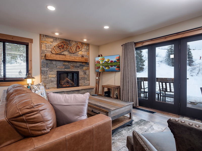 Curl up by the stone fireplace with your favorite book, or enjoy ski slope views from the balcony—this cozy living room invites you to unwind in mountain luxury.