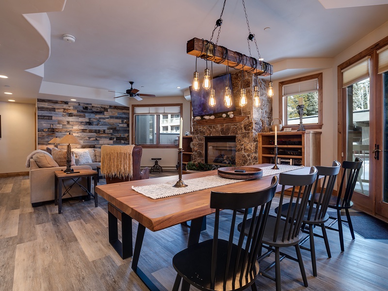 Gather around this stunning handcrafted table where rustic wood meets modern comfort. Natural light pours through expansive windows while the stone fireplace adds warmth to your mountain retreat.