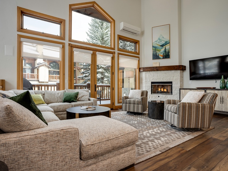 Unwind in your sunlit living room where soaring windows frame alpine views, a cozy fireplace crackles nearby, and plush seating invites you to relax after a mountain adventure.