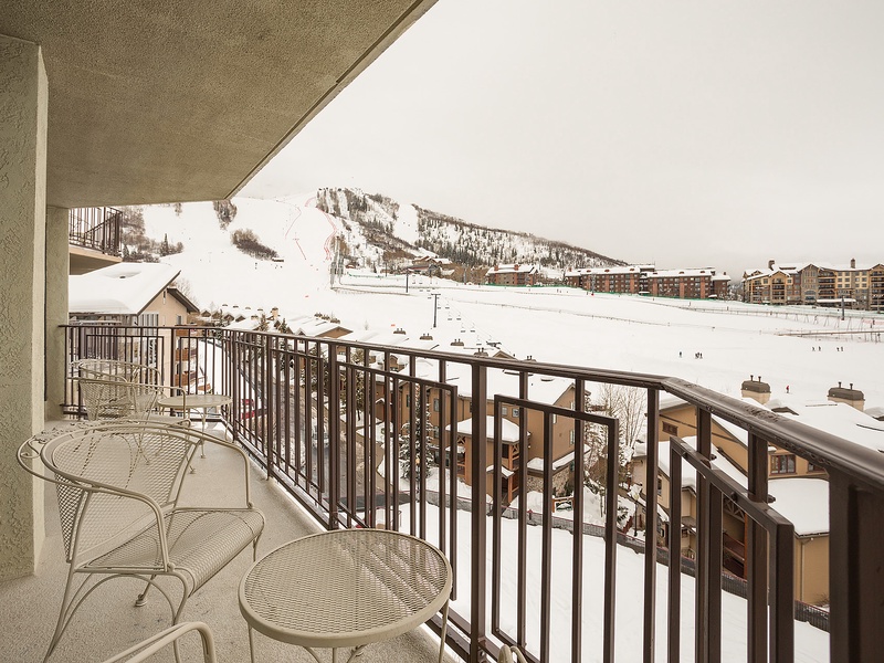 This expansive balcony frames a striking winter panorama of ski slopes, chairlifts, and alpine lodges. A scenic mountain resort setting awaits outside the property, perfect for winter sports enthusiasts.