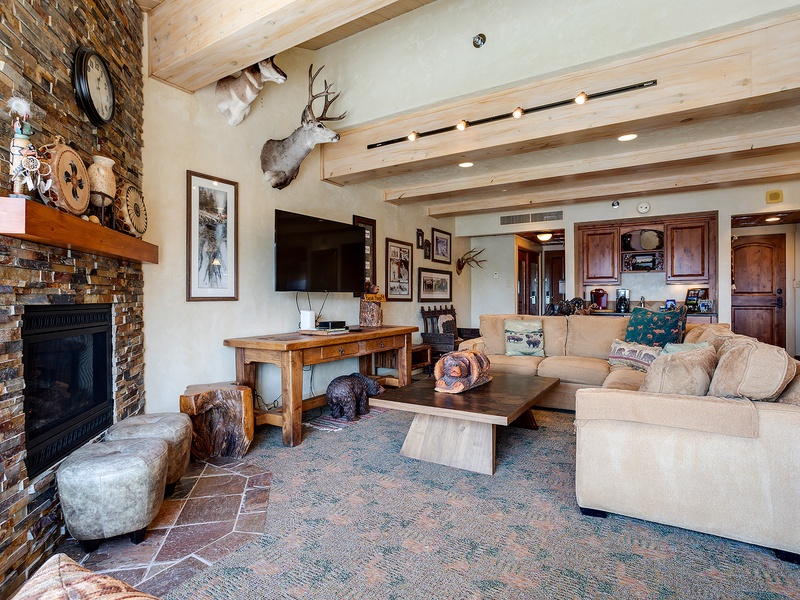 Picture yourself unwinding in this spacious living room, where rustic charm meets mountain luxury. Sink into plush sofas by the stone fireplace and enjoy your favorite shows on the flat-screen TV under vaulted wood-beam ceilings.