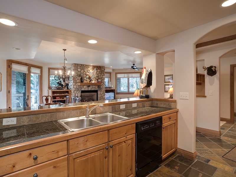 Cook up your favorite meals in this spacious kitchen with granite counters, a double sink, and dishwasher, all while enjoying the cozy stone fireplace and mountain views beyond.