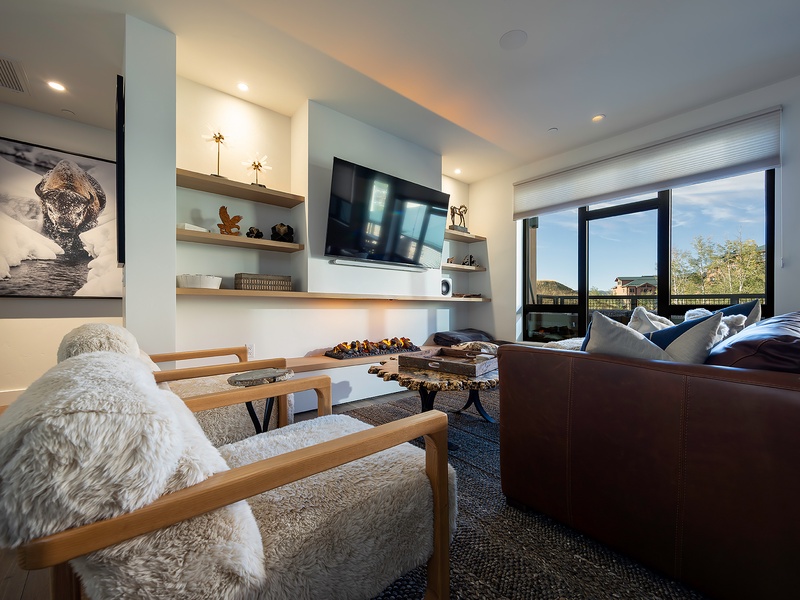 Sink into plush leather and cozy textures in this modern living room, where open shelving displays personal touches and floor-to-ceiling windows frame sweeping views of the surrounding landscape. Your perfect retreat awaits.