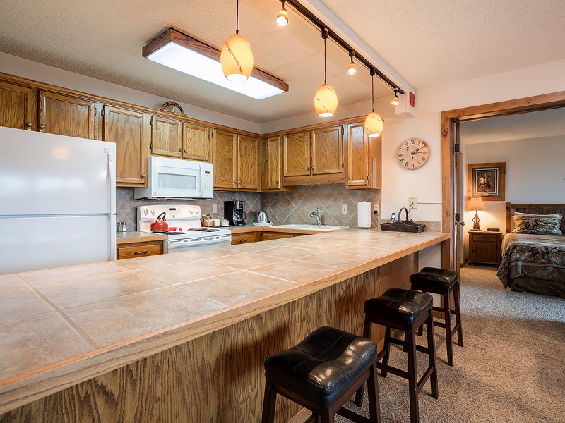 Picture yourself preparing meals in this well-equipped kitchen with warm wood cabinetry, tiled counters, full appliances, and a spacious breakfast bar for casual dining.