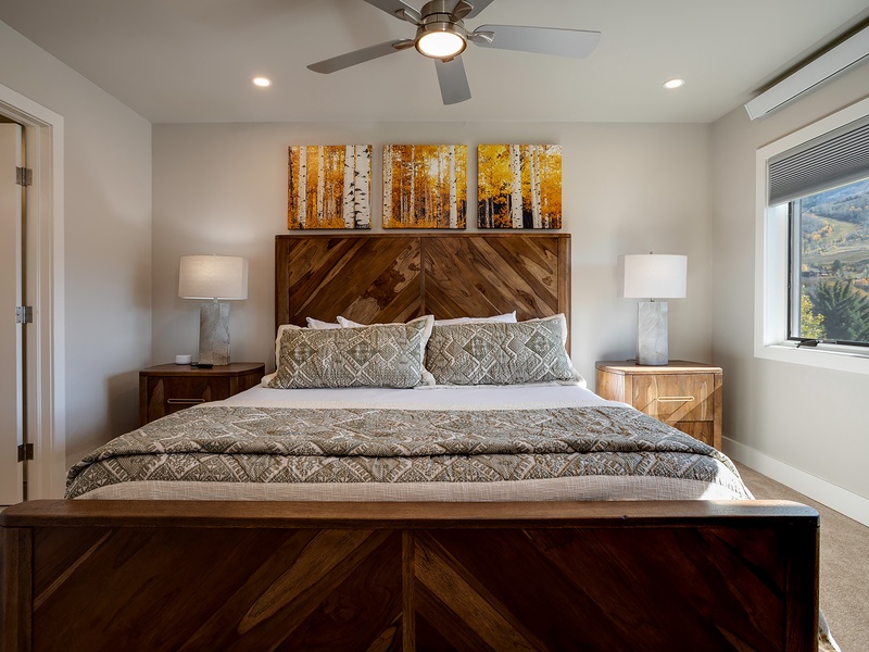 Drift off in this serene bedroom with a plush bed, warm wood accents, soft lighting, and stunning views framed by the window—your restful retreat awaits.