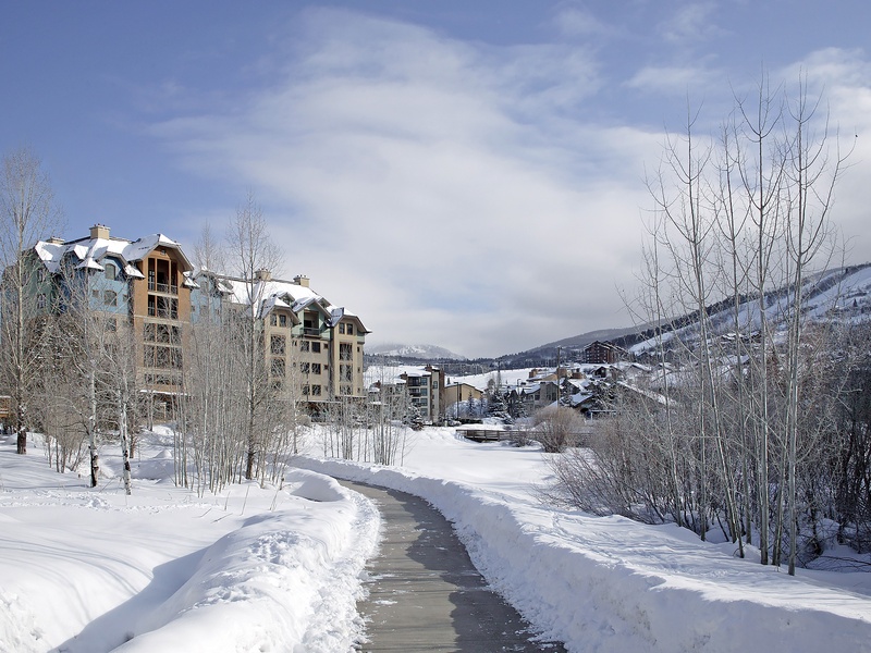 A pristine winter mountain village nestled among snow-covered peaks and aspens, offering scenic access to slopes and alpine charm.
