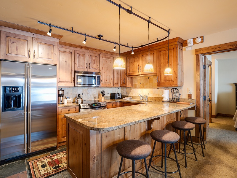 Gather around the spacious granite island with room for everyone. Warm wood cabinetry, stainless steel appliances, and pendant lighting create a welcoming space to cook, share meals, and make memories together.