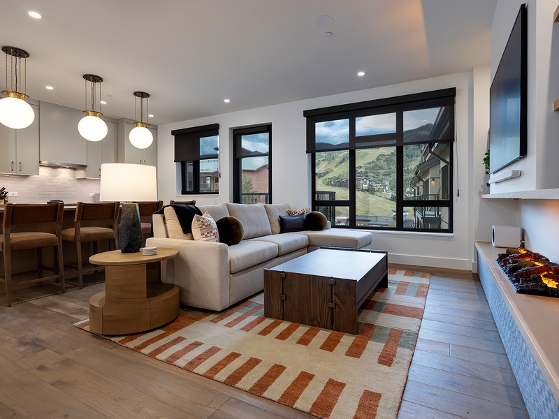 Sink into the plush sectional and drink in sweeping mountain views through floor-to-ceiling windows. Modern pendant lights and a cozy fireplace create your perfect alpine retreat.