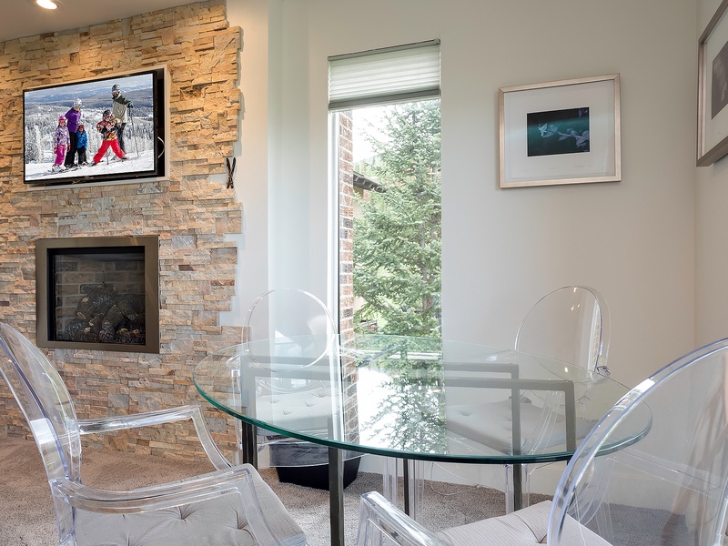Gather around the sleek glass table by the stone fireplace, with mountain views and modern seating creating your perfect spot for meals and après-ski stories.