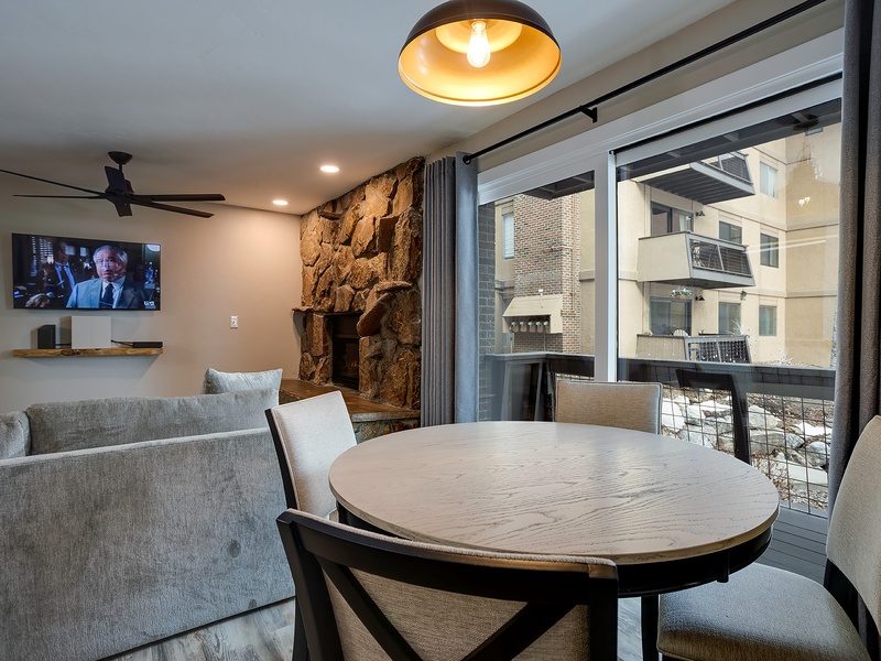 Unwind at your round dining table with mountain views and a cozy stone fireplace. Sunlight streams through floor-to-ceiling windows, illuminating your open-concept space designed for effortless comfort.