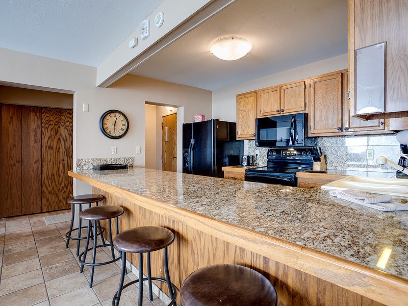 Gather around your spacious granite breakfast bar where morning coffee feels effortless. The fully equipped kitchen invites you to cook together, with sleek black appliances and plenty of counter space for meal prep and conversation.